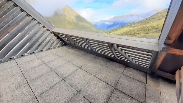 A stone-tiled floor and a wooden railing with a view of a mountainous landscape.