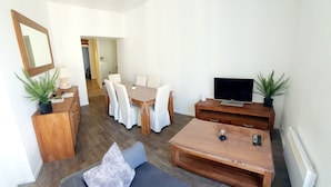 Een moderne woonkamer met een bank, salontafel, televisie, eettafel, stoelen en potplanten.