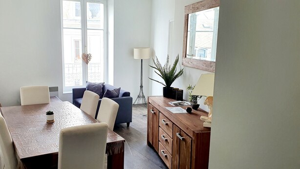 Een eetgedeelte met een houten tafel, witte stoelen, een blauwe bank en een houten kast.