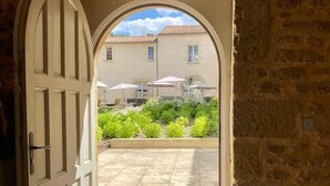 An open doorway leading to a courtyard with a tiled floor, a stone wall, and a building with a tiled roof in the background. - Château Toulouse-Lautrec Malromé (Saint-André-du-Bois)