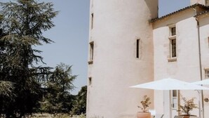 A swimming pool with lounge chairs and umbrellas, a tower with a conical roof, and a building with windows. - Château Toulouse-Lautrec Malromé (Saint-André-du-Bois)
