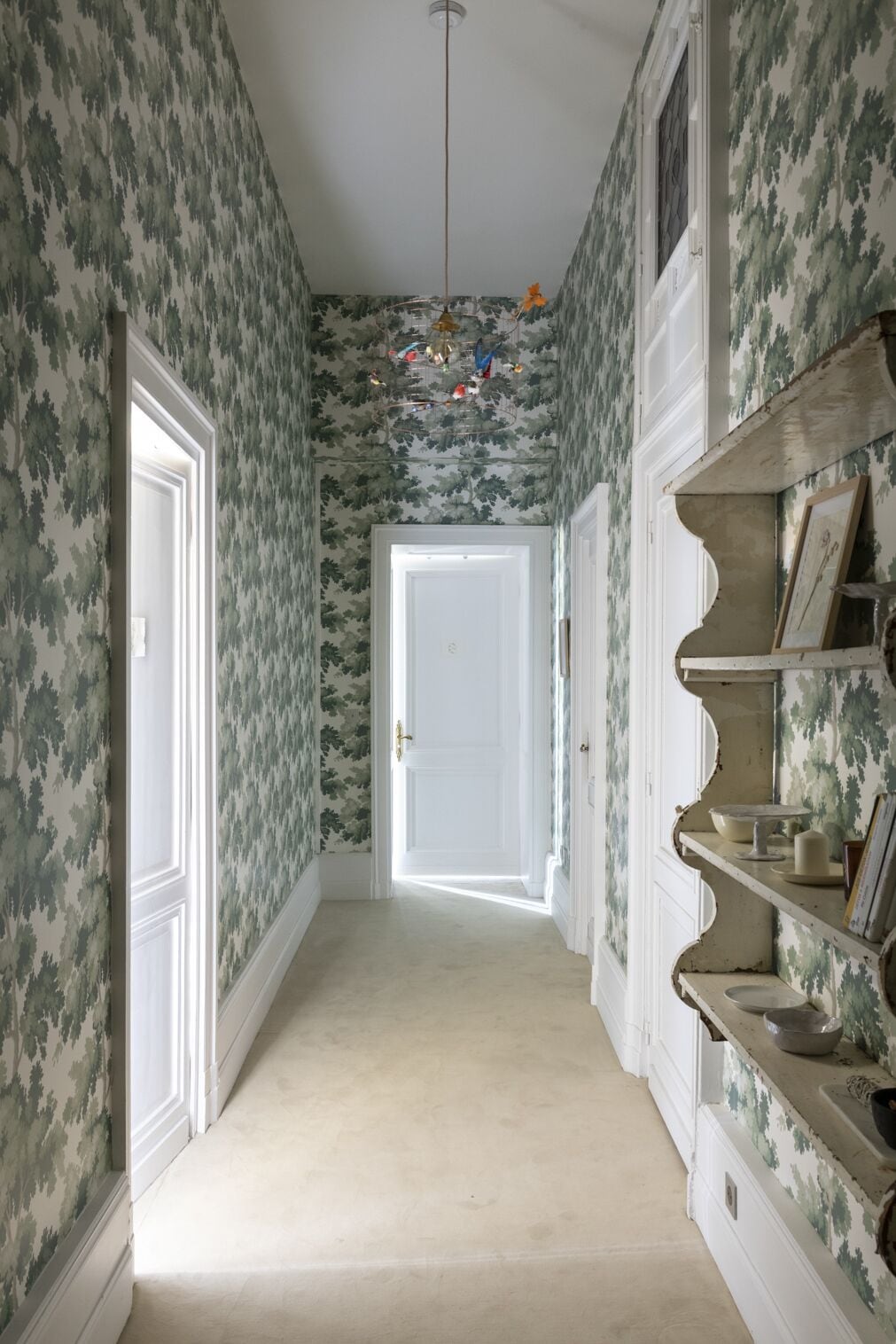 Ein Flur mit ornamentalem Wandpapier, einer weißen Tür am Ende und einem Regal mit Dekorationen.