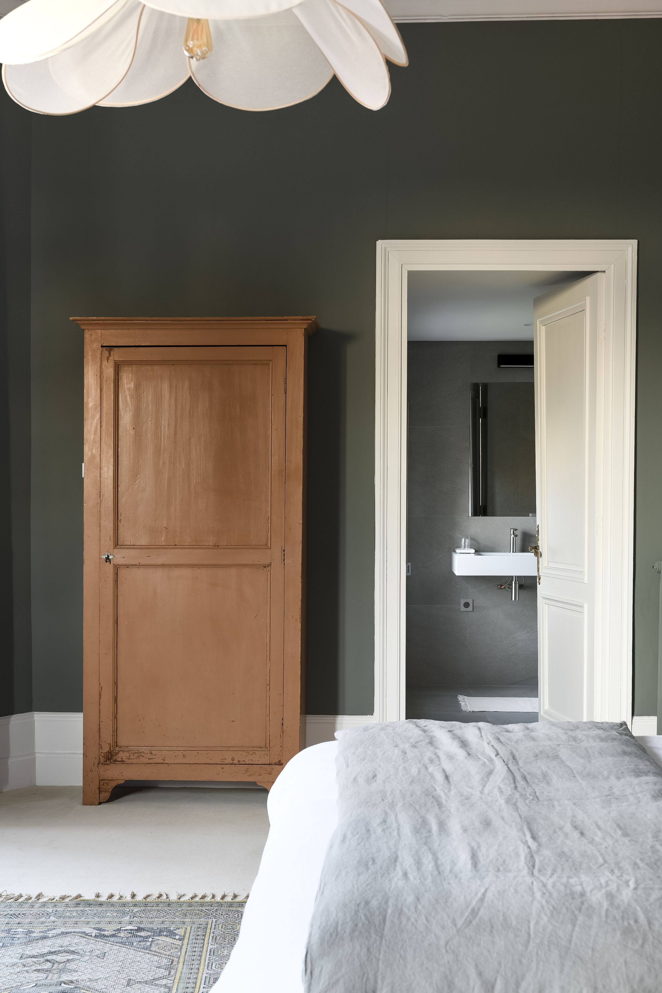Une chambre à coucher avec un grand lit, une armoire en bois et une salle de bain visible à travers une porte ouverte.