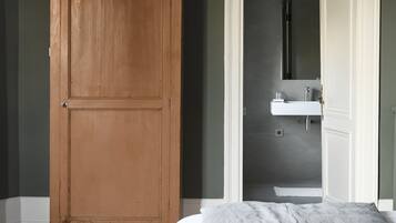 Une chambre à coucher avec un grand lit, une armoire en bois et une salle de bain visible à travers une porte ouverte.