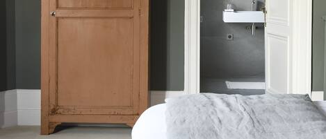 Un dormitorio con una cama grande, un armario de madera y un baño que se ve a través de una puerta abierta.