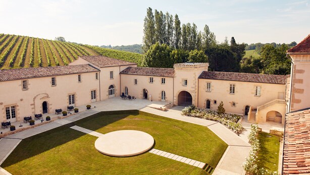 A courtyard with a central lawn, surrounding buildings with tiled roofs, and a vineyard in the background. - Château Toulouse-Lautrec Malromé (Saint-André-du-Bois)