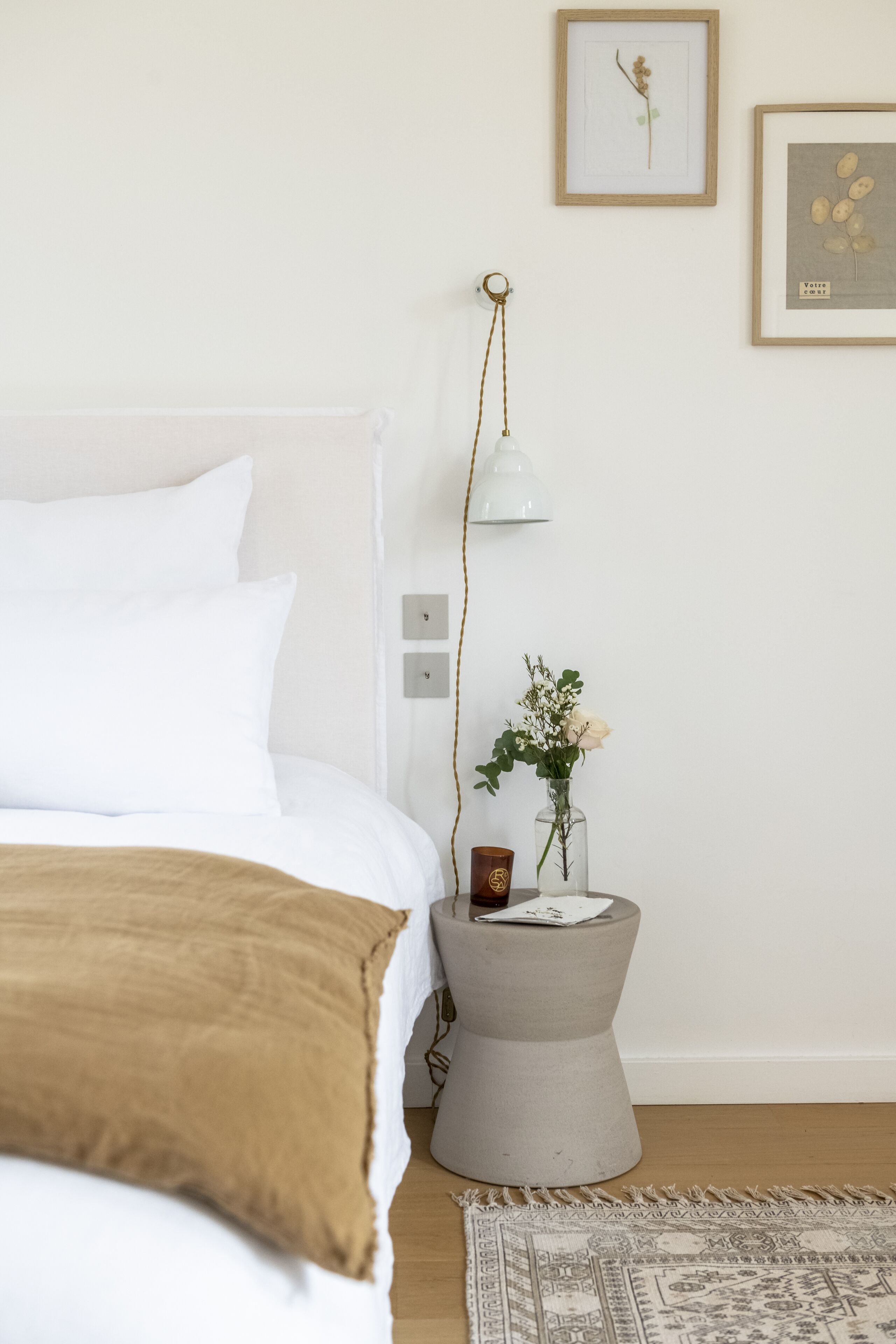 A neatly arranged bedroom with a bed, bedside table, lamp, and framed pictures on the wall.