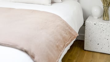 Une chambre à coucher bien rangée, avec un grand lit, du linge de lit blanc et une petite table de chevet ornée d’un vase de fleurs séchées.