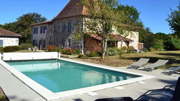 A stone building with a swimming pool and lounge chairs.