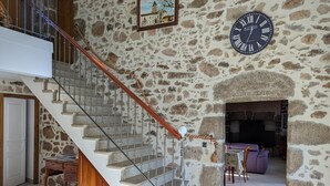 A stone-walled interior with a staircase, a clock, and a fireplace.