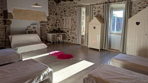 A cozy bedroom with a stone wall, wooden ceiling beams, a bed, a desk, and two small cabinets with heart decorations.