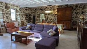 A spacious living room with a stone wall, a purple sofa, a wooden coffee table, and a dining area with a wooden table and chairs.