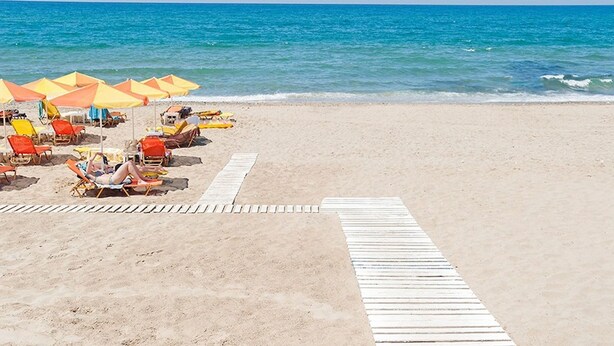 A beach with sun loungers and umbrellas, a wooden walkway, and the ocean in the background.
