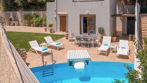A modern outdoor pool area with lounge chairs, a dining table, and a barbecue grill.
