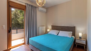 A bedroom with a bed, a nightstand, a lamp, an air conditioning unit, a window with curtains, and a view of trees outside.