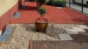 Ein Innenhof mit einem roten Kiesweg, einem großen Pflanzkübel mit einem Baum und einem Gebäude mit mehreren Fenstern.