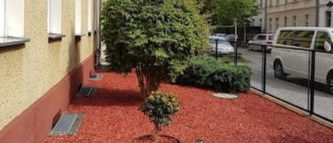 A courtyard with a red gravel path, a large planter with a tree, and a building with multiple windows.
