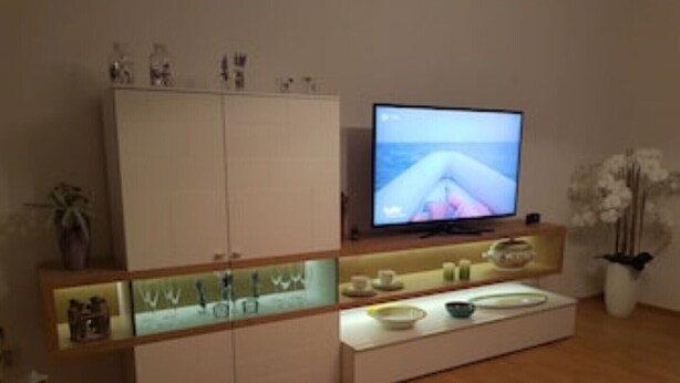 Ein modernes Wohnzimmer mit Fernseher, Holzschränken und einer Glasvitrine.