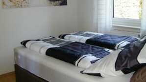 Ein Schlafzimmer mit zwei Betten, einem Strandbild an der Wand und einem Fenster mit Vorhängen.