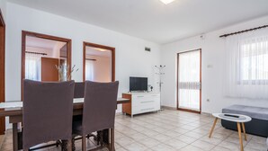 A modern living room with a dining area, a sofa, a TV, and a small table. - Apartment Susa (Vir)