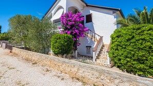 A white building with a staircase leading to a balcony, surrounded by greenery and a clear blue sky. - Apartment Susa (Vir)