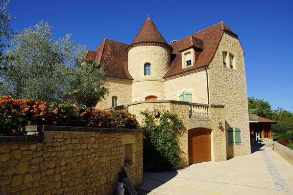 A stone building with a turret and a round tower, featuring a stone wall and a paved entrance.