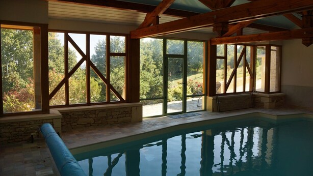 An indoor swimming pool with stone walls and large windows. - Apartment with swimming pool and place of relaxation and leisure (Sarlat-la-Canéda)