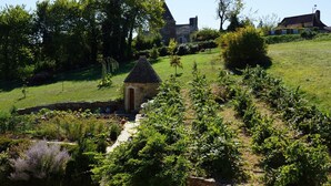 A stone building with a thatched roof, surrounded by a lush garden and a large tree. - Apartment with swimming pool and place of relaxation and leisure (Sarlat-la-Canéda)
