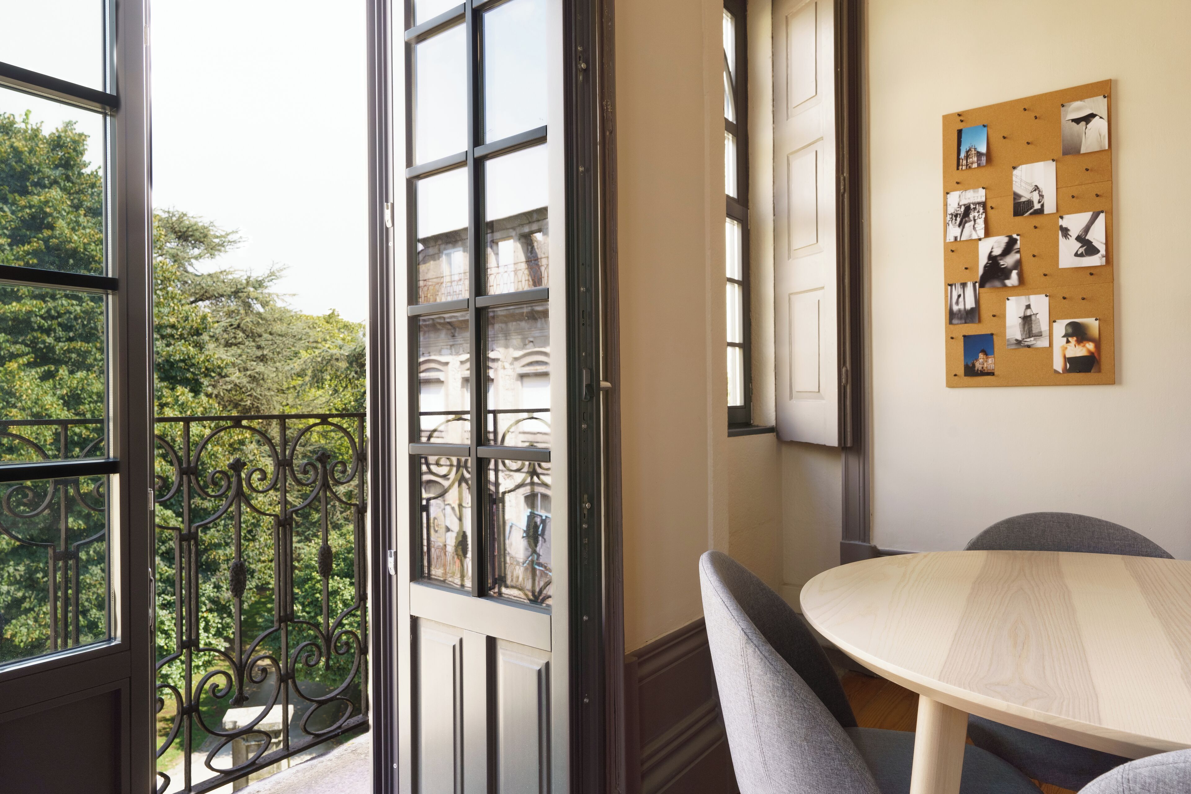 A room with a balcony, a corkboard with photos, and a round table.
