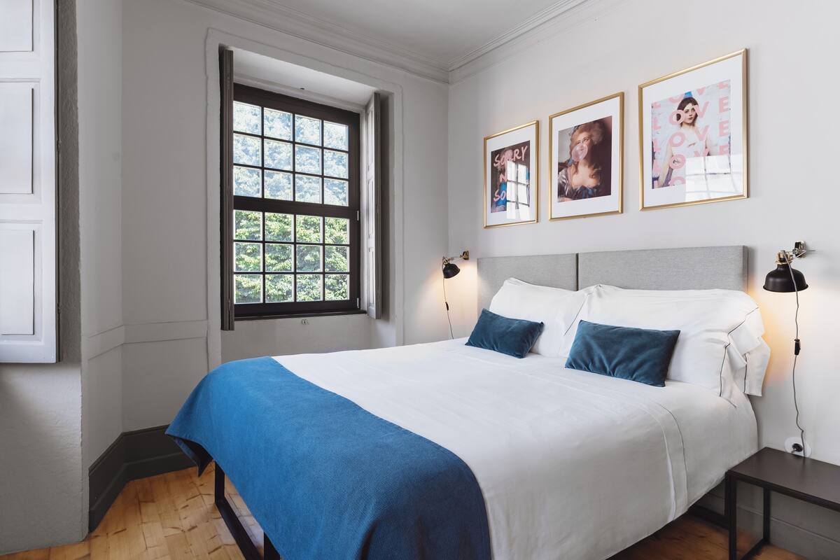 A neatly made bed with a blue throw blanket, a bedside lamp, and framed pictures on the wall.