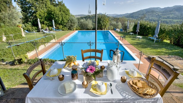 Une table à manger installée à l’extérieur, offrant une vue sur une piscine et des montagnes.
