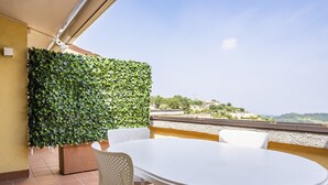 A terrace with a white table and chairs, a green leafy wall, and a view of a hillside. - Lisa's Apartment (Muscoline)