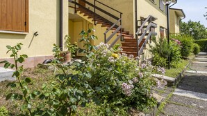 A two-story house with a staircase leading to the upper floor, surrounded by a garden with various plants and flowers. - Lisa's Apartment (Muscoline)