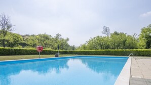 Een rechthoekig zwembad met een helderblauw wateroppervlak, omringd door een lage haag en een verhard pad.
