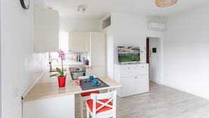 Cozinha compacta com armários brancos, bancada de madeira e um pequeno espaço de refeições com uma cadeira vermelha e uma mesa.