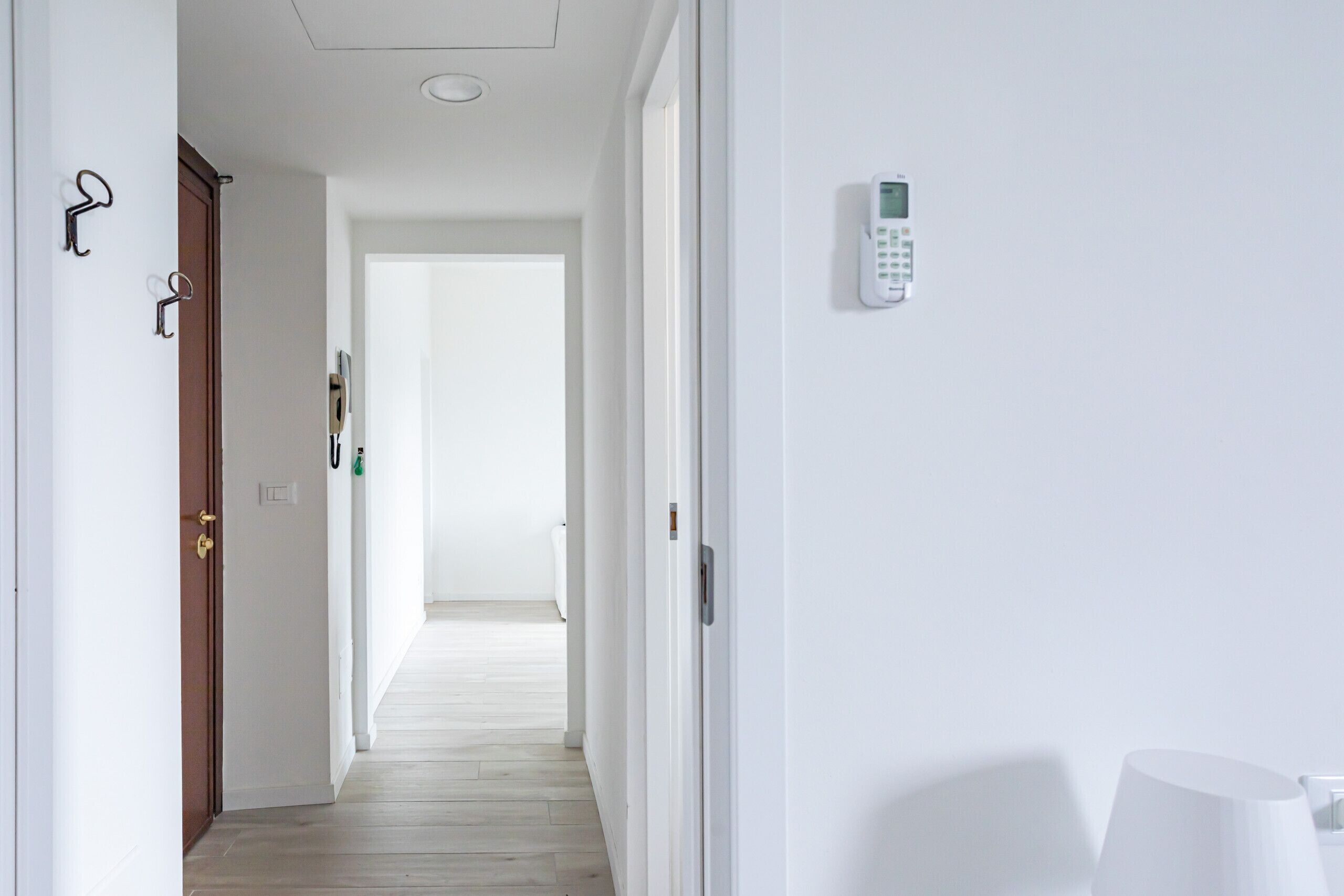 A hallway with a door on the left, a wall-mounted intercom on the right, and a lamp on the far wall.