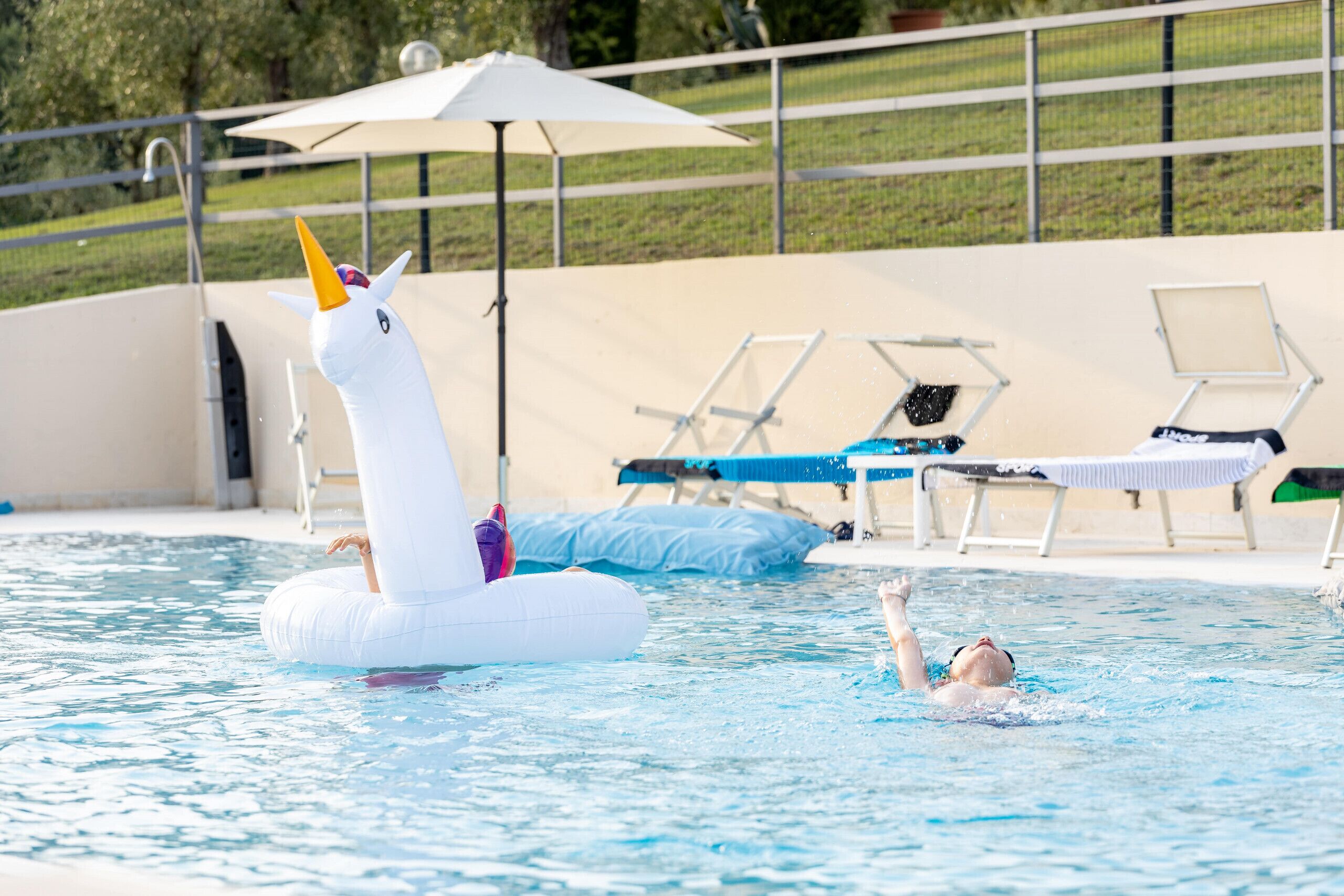 Ein Swimmingpool mit aufblasbaren Einhorn-Schwimmanhängern, Liegestühlen und Sonnenschirmen.