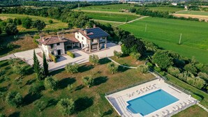 Une grande maison avec une piscine, entourée de champs verdoyants et d’arbres.