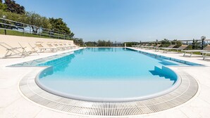 Une grande piscine aux eaux claires, de forme circulaire, entourée d’une terrasse.