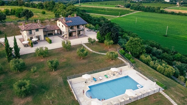 Une grande maison avec une piscine, entourée de champs verdoyants et d’arbres.