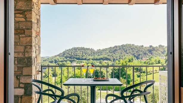 Ein Balkon mit Tisch und Stühlen, eine Steinmauer und Blick auf eine grüne Landschaft.