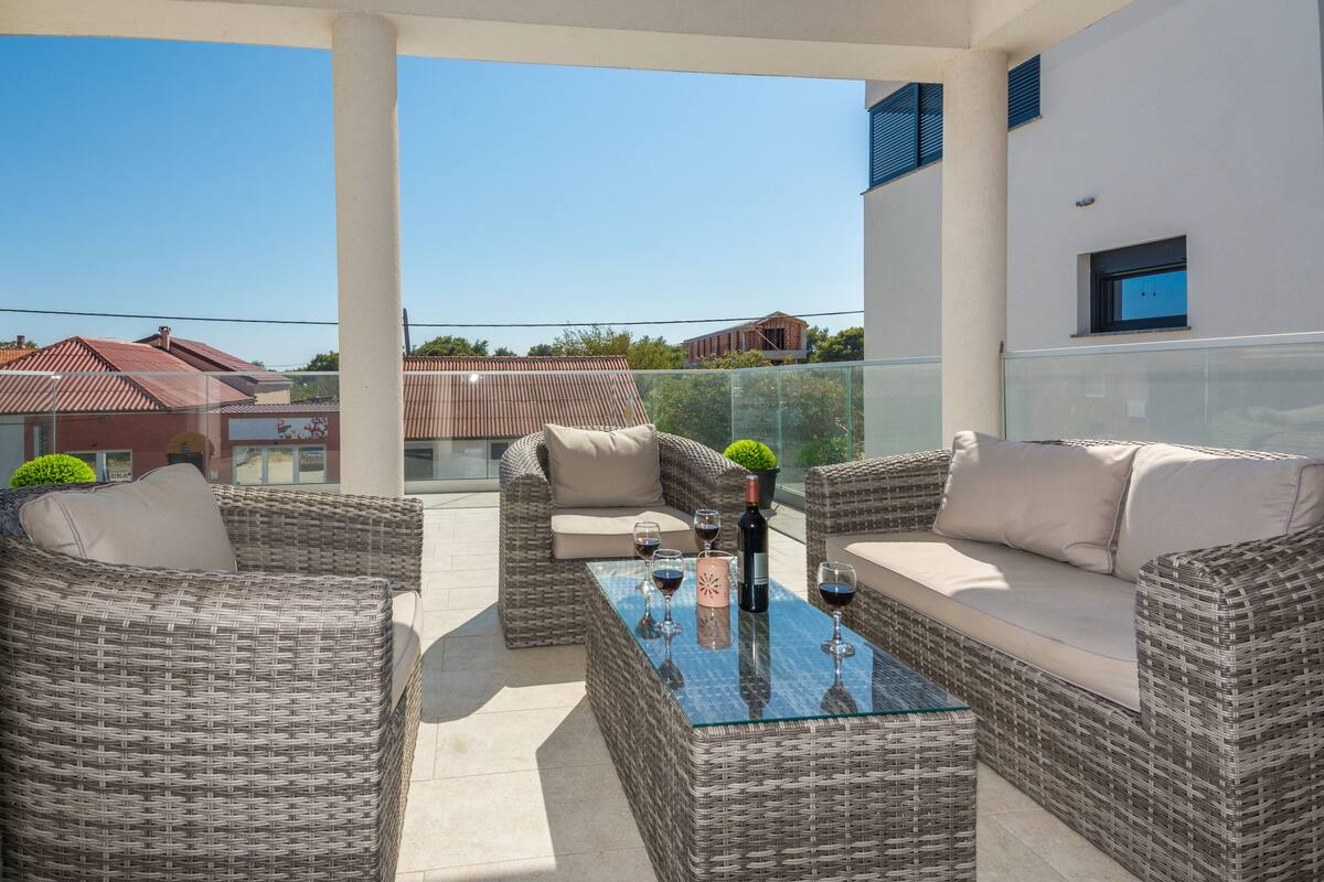 A balcony with wicker furniture, a glass table, and wine glasses.