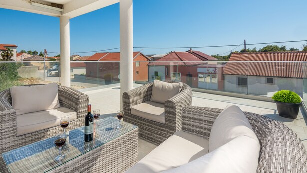 A balcony with wicker furniture, a glass table, and a bottle of wine. - Apartments Krpan (Vir)