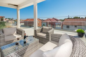 A balcony with wicker furniture, a glass table, and a bottle of wine. - Apartments Krpan (Vir)