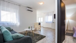 A modern living room with a sofa, a small table, and a chair. There is a kitchen area visible through an open door. - Apartments Krpan (Vir)
