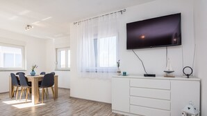 A modern living room with a dining area, a flat-screen TV mounted on the wall, and a white cabinet with drawers. - Apartments Krpan (Vir)
