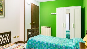 Ein Schlafzimmer mit zwei Betten, einer grünen Wand, einem weißen Kleiderschrank und einem hölzernen Kopfteil.