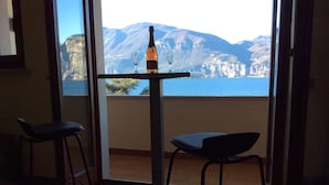 Una stanza con un tavolo apparecchiato per due, una bottiglia di vino e due sedie. Un'ampia finestra offre vista sulle montagne e sul mare.