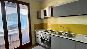 Una cucina moderna con piano cottura a gas, forno e lavello, e una porta vetrata scorrevole che dà su un balcone.