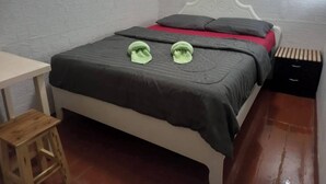 Ein Einzelbett mit weißem Kopfteil, einem Holznachttisch und einem kleinen Hocker.
